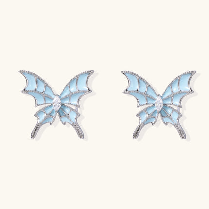 Long silver-tone earrings with powder blue enamel butterfly studs and flowing chain tassels on cream background