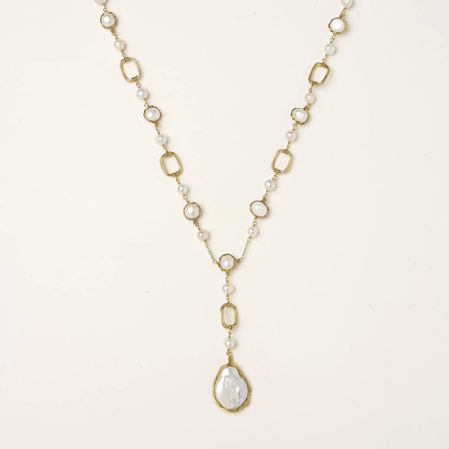 Y-shaped gold necklace with alternating geometric links, freshwater pearls, and baroque pearl pendant on cream background