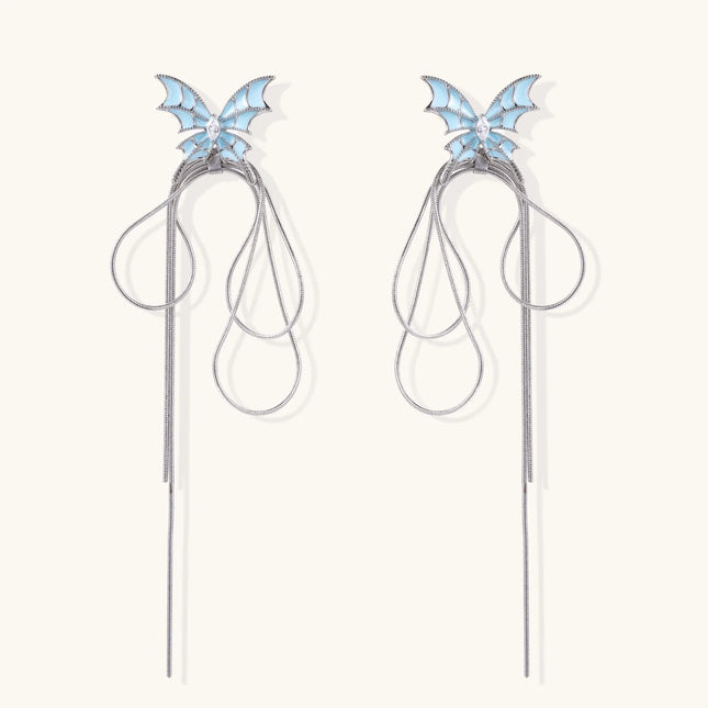 Long silver-tone earrings with powder blue enamel butterfly studs and flowing chain tassels on cream background
