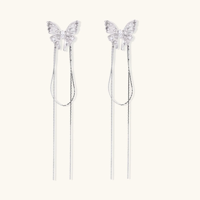 Pair of silver threader earrings with crystal butterfly tops and long chain drops on cream background.