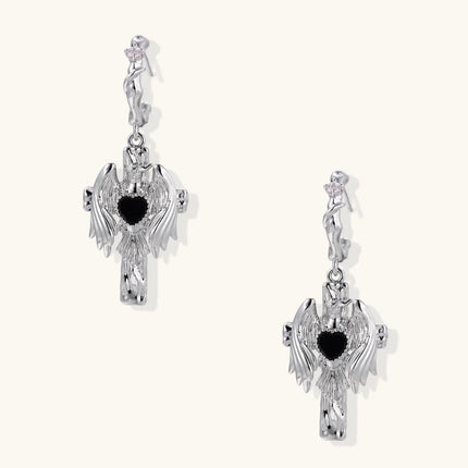 Silver drop earrings with twisted hoops and angel wings embracing black heart locket on white background.