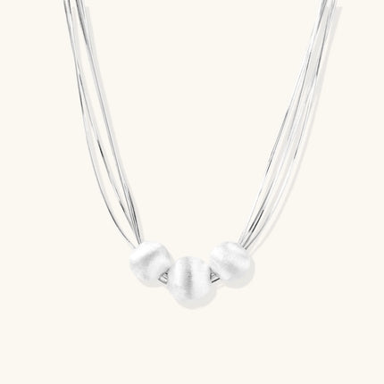 Sterling silver multi-strand necklace with three brushed round beads on cream background