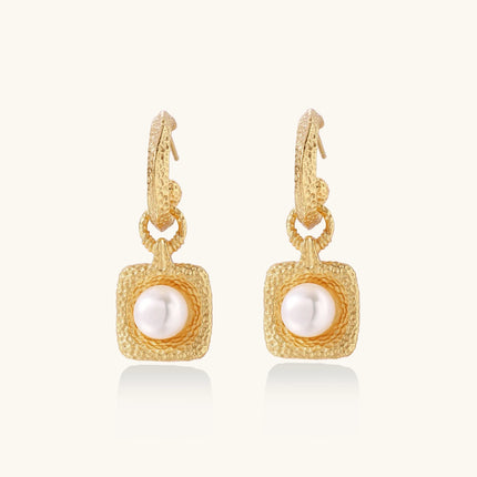 Pair of gold vermeil hoop earrings with textured square frames holding freshwater pearls on cream background
