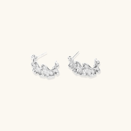 White gold plated sculptural hoop earrings with organic wavy edges and reflective metallic finish on cream background