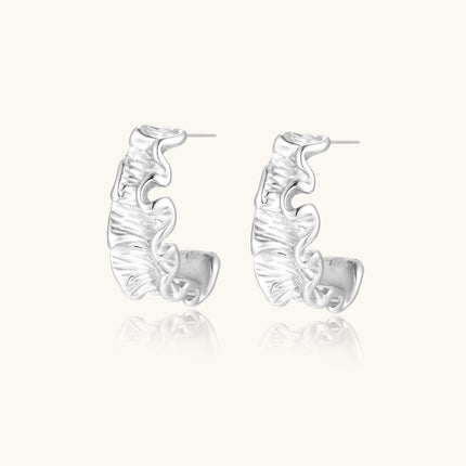 White gold plated sculptural hoop earrings with organic wavy edges and reflective metallic finish on cream background
