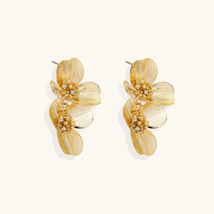 Pair of gold-plated double flower earrings with textured petals and crystal centers on cream background.