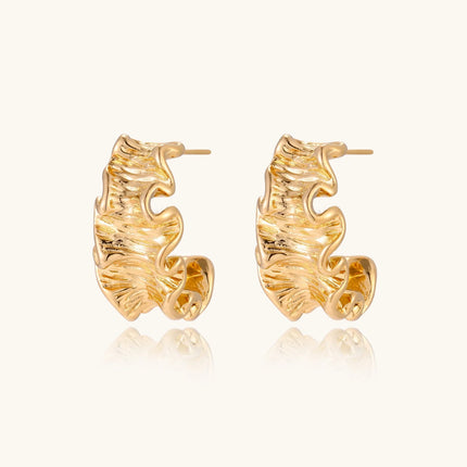 Pair of gold huggie hoops with sculpted wave texture and dimensional ripples on neutral background.