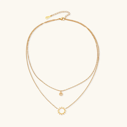 Gold layered necklace set with sunburst and smiley face pendants on delicate chains against white background.