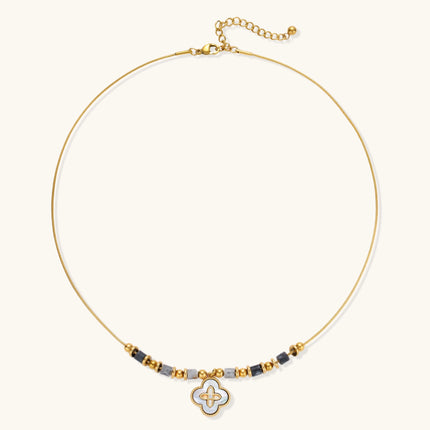 Gold-toned beaded necklace with grey stones and quatrefoil abalone shell pendant on cream background.