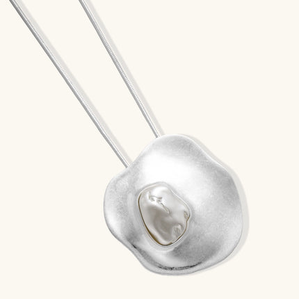 Organic-shaped gold pendant necklace with baroque pearl accent on adjustable chain, displayed against neutral background.